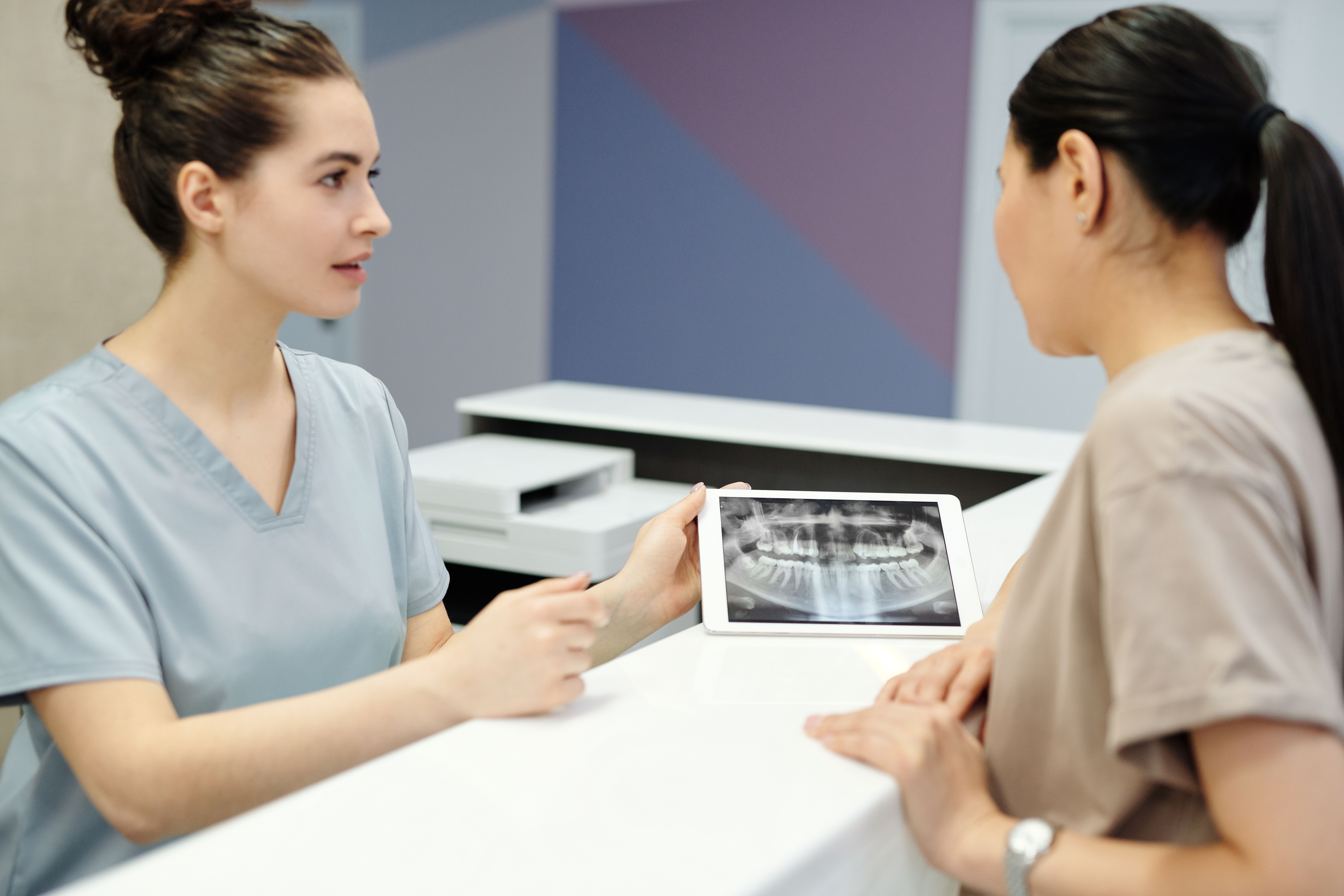 A dentist shows a patient a dental X-ray on a tablet in a clinic.