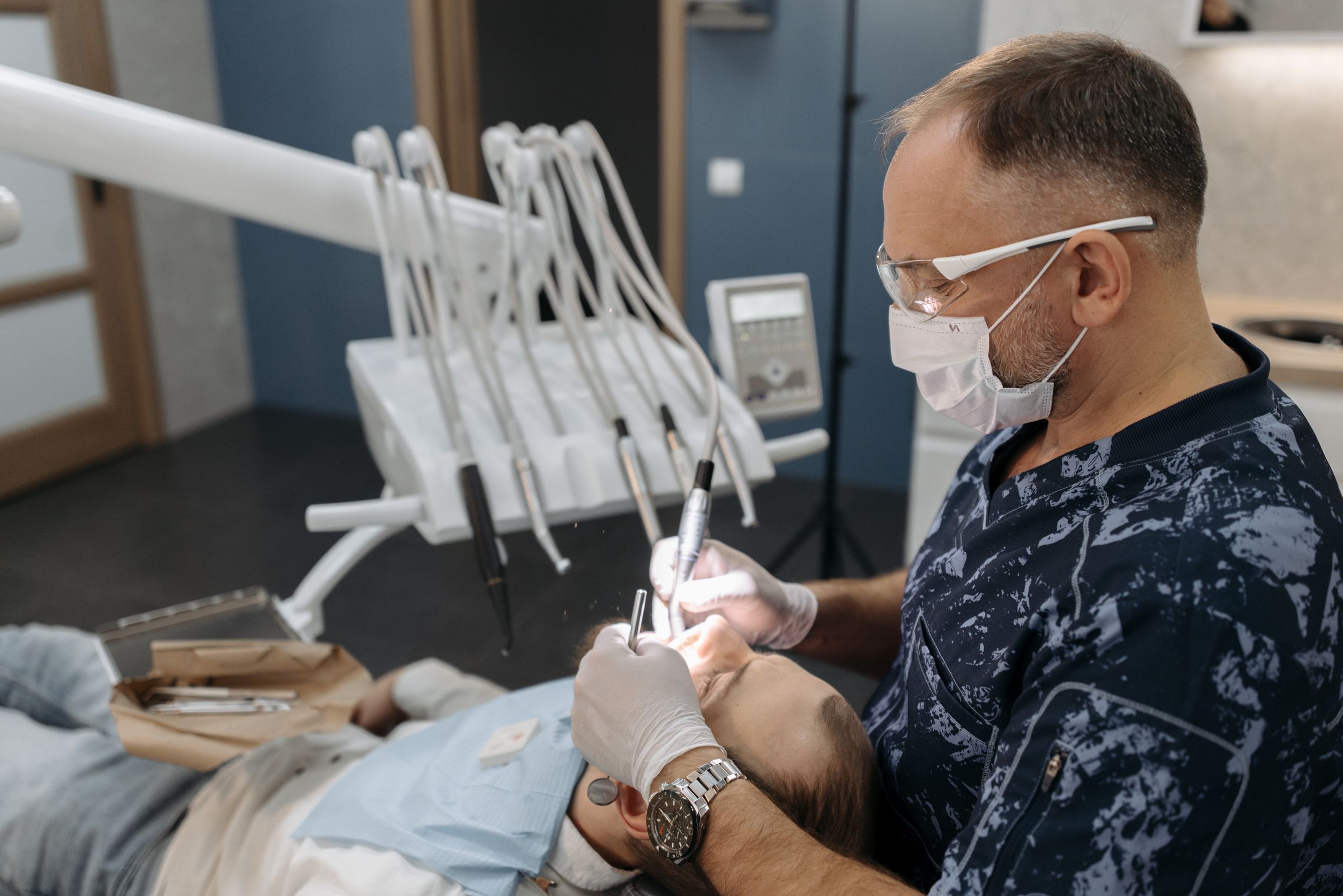 A dentist closely examines a patient's teeth with a handpiece in a dental chair.